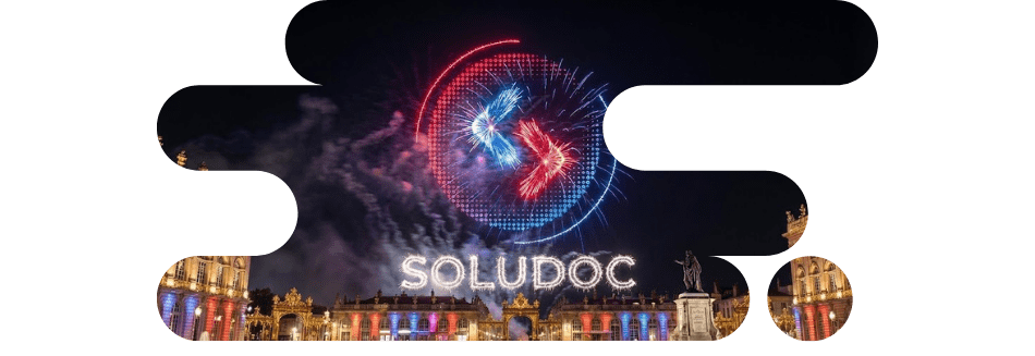 Spectacle nocturne sur la Place Stanislas à Nancy illuminée en bleu, blanc et rouge, avec le nom "SOLUDOC" et son logo stylisé apparaissant en light painting et feux d'artifice dans le ciel. Partenaire solutions numériques globales